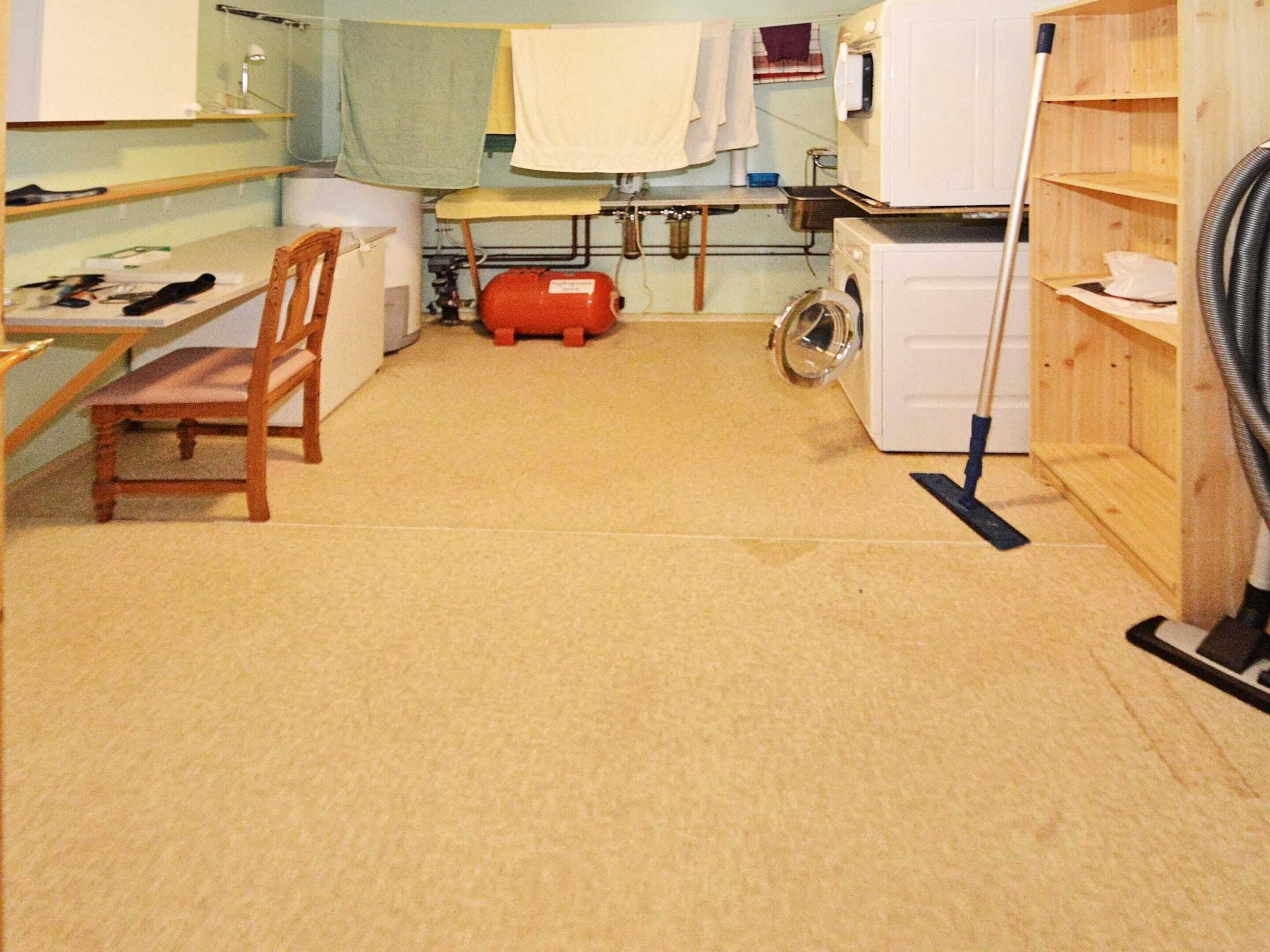 Una sala de lavandería con lavadora, secadora, tabla de planchar y una silla.