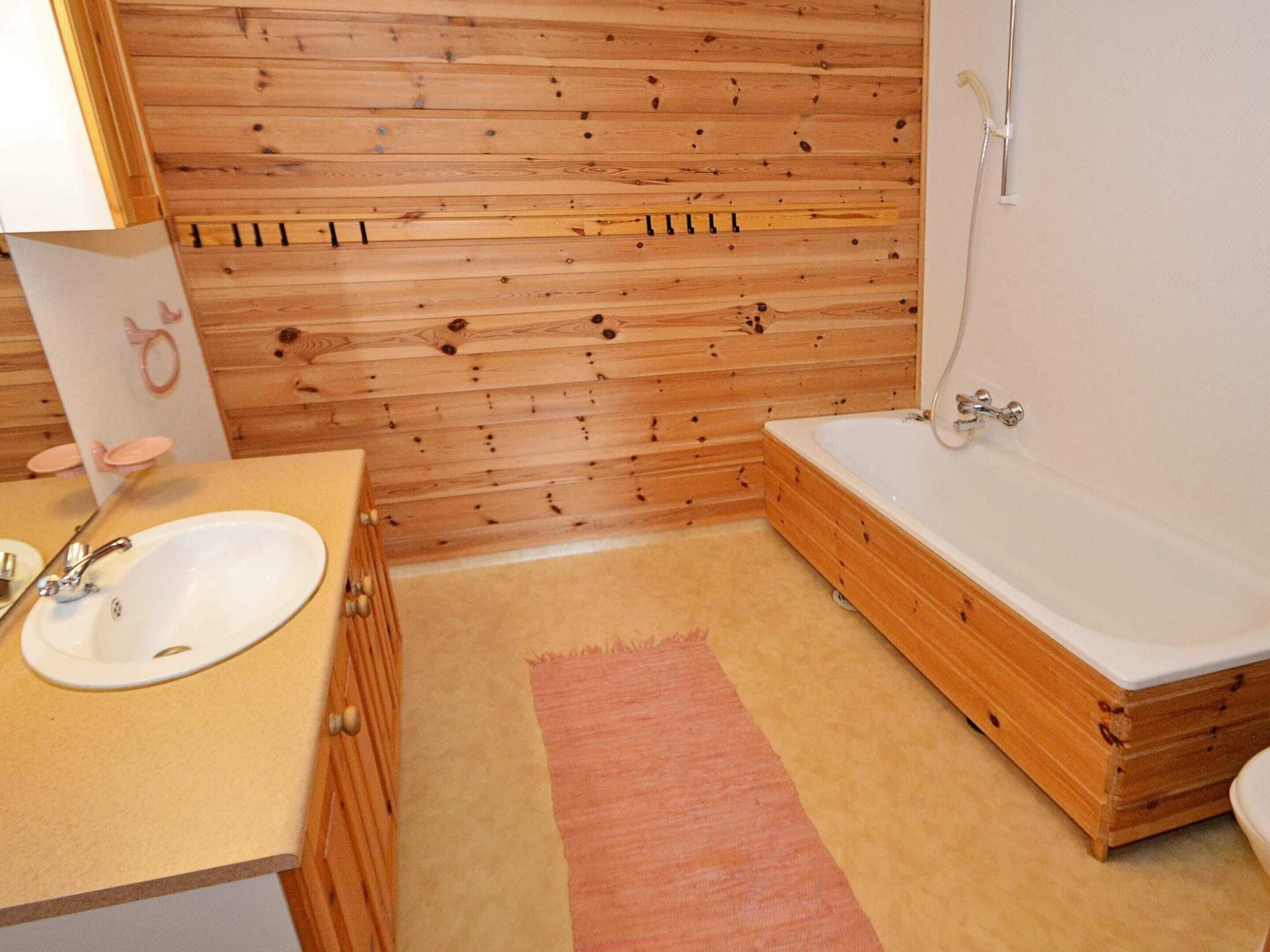 Un bagno con rivestimenti in legno, un lavandino, una vasca da bagno e una doccia.