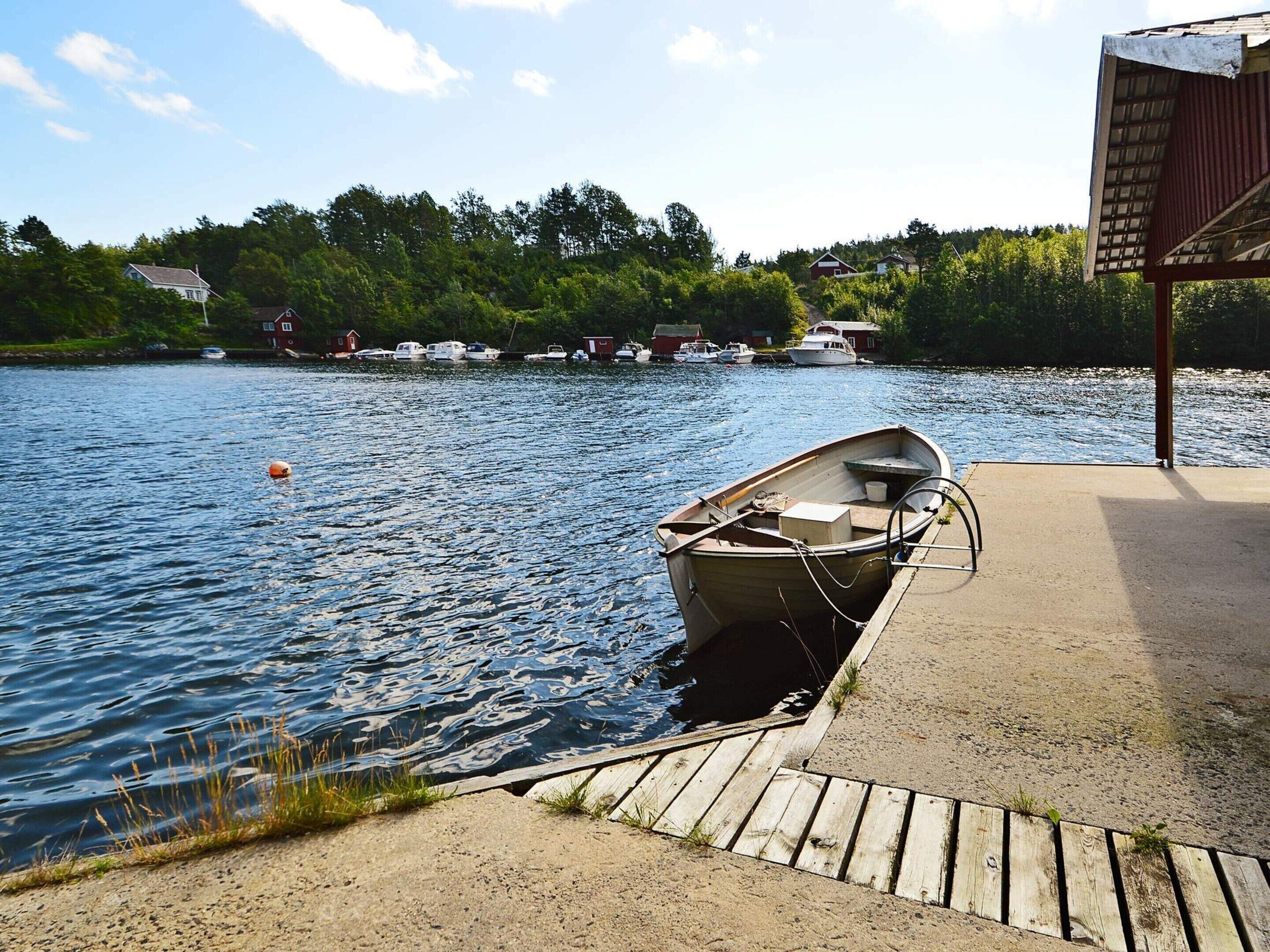 A small wooden boat docked at a concrete pier with a sandy shore and a forested background.