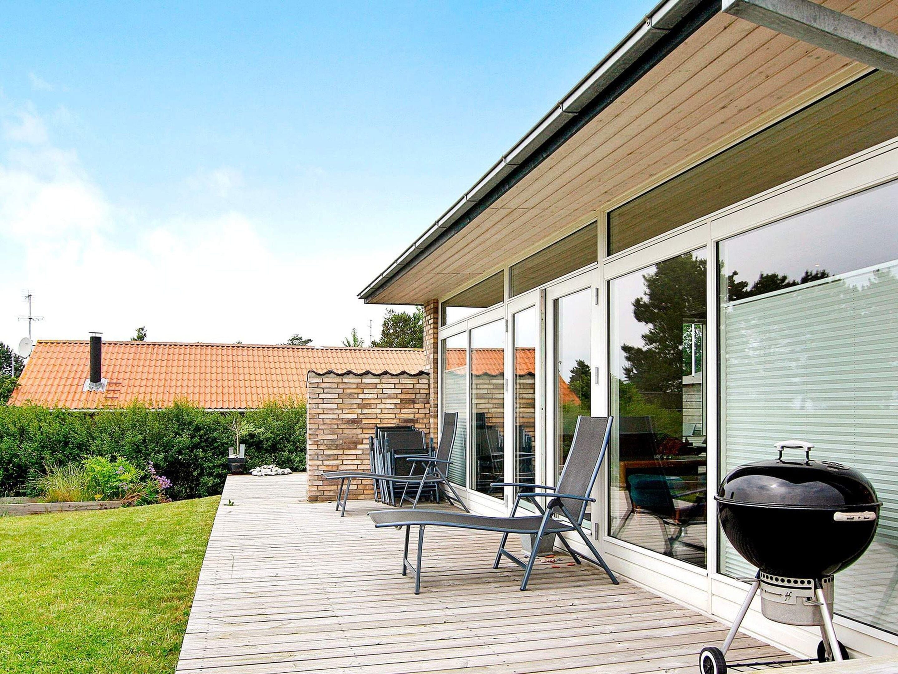 Een terras met een barbecue, tuinmeubilair en uitzicht op een gebouw van baksteen.