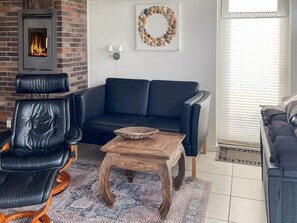 A living room with a brick fireplace, a black leather sofa, a wooden coffee table, and a patterned rug.