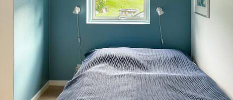 A bedroom with a bed, a window with a view of a garden, and two wall-mounted lamps.
