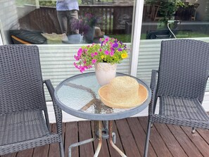 A round glass table with two wicker chairs, a woven hat, and a potted plant with pink and yellow flowers. - 5 Star Holiday Home in Sydals (Sydals)
