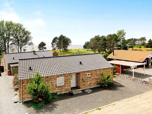 Un bâtiment de plain-pied en briques, avec un toit en tuiles, un garage et un espace extérieur abrité.