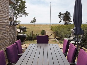 A patio with a table and chairs, a grill, and a view of the sea.