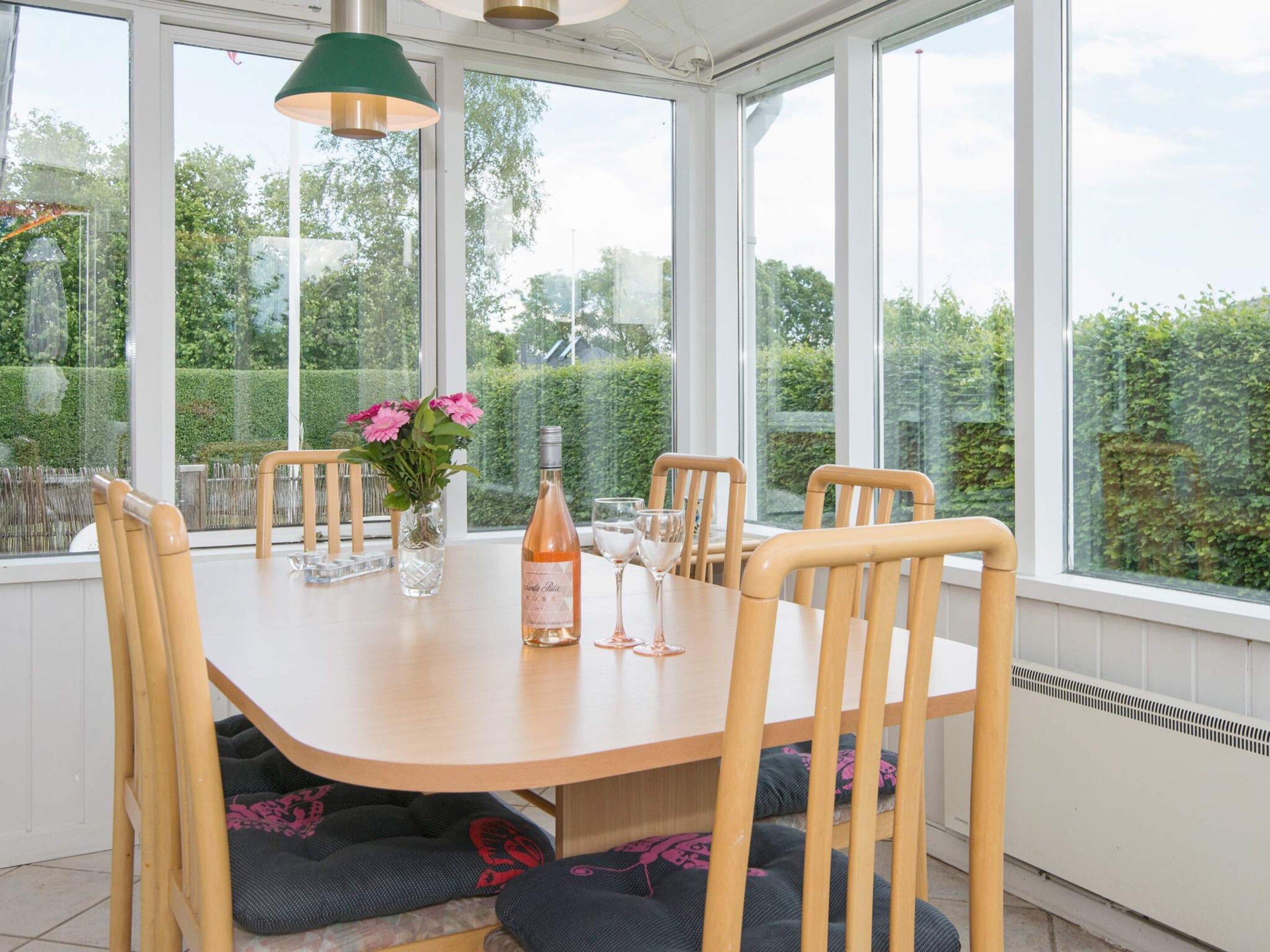 A dining area with a table, chairs, a bottle of wine, and a vase of flowers.