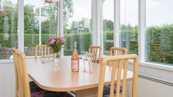 A dining area with a table, chairs, a bottle of wine, and a vase of flowers.