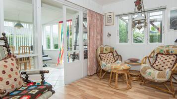 A room with a wooden floor, wicker chairs, a sofa, and a dining table.