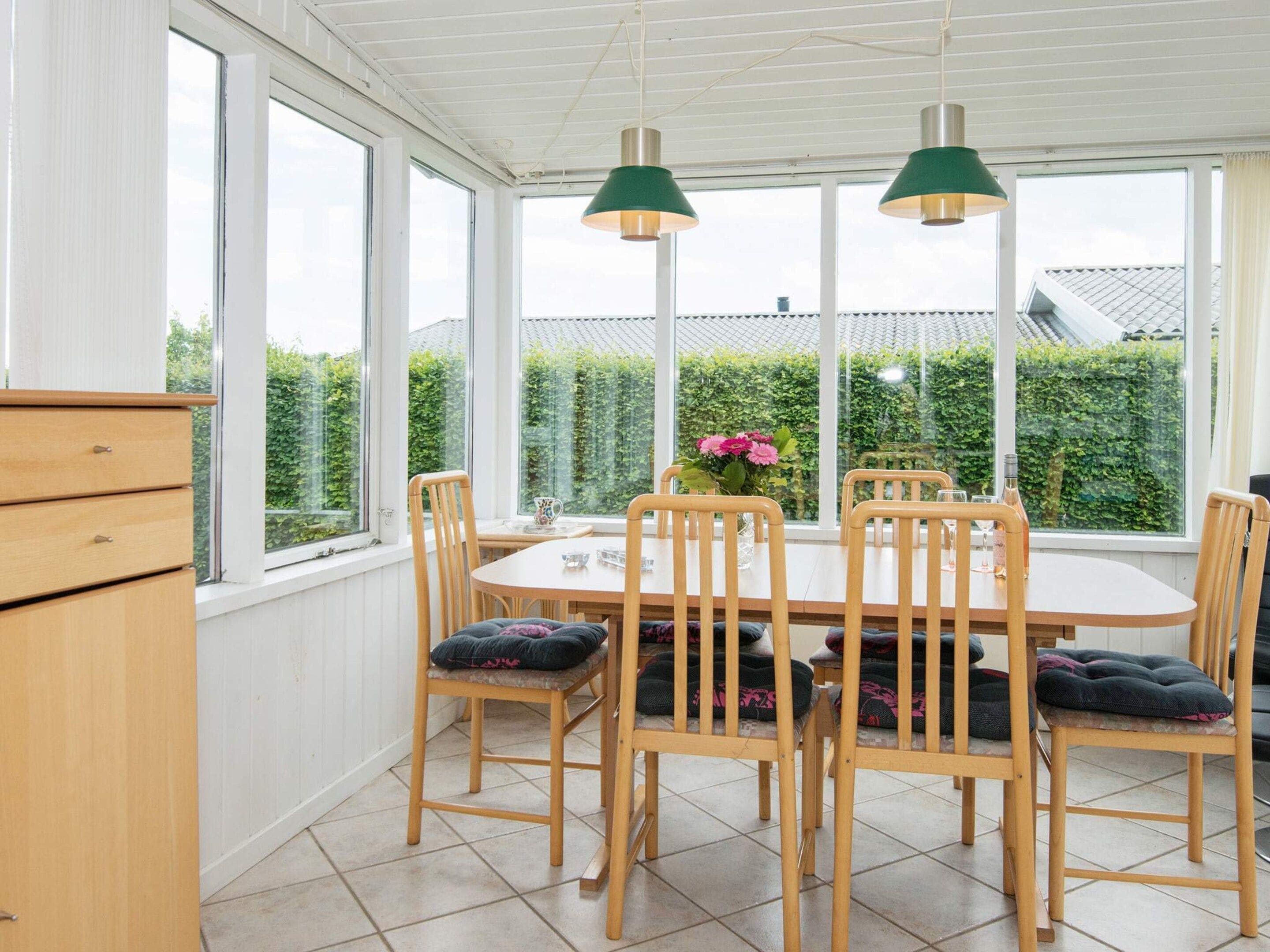A conservatory with a dining table, chairs, and pendant lights.