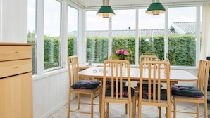 Ein Wintergarten mit Esstisch, Stühlen und Pendelleuchten.