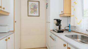 A compact kitchen with white cabinets, a coffee maker, and a sink.