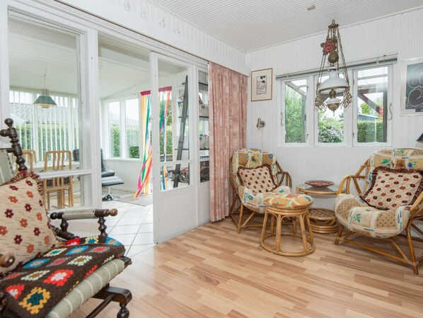 A cozy room with a wooden floor, wicker chairs, a patterned sofa, and a large window with curtains.