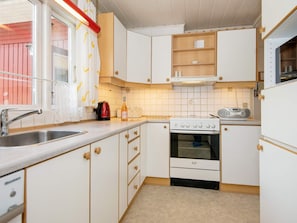Cocina compacta con armarios blancos, estufa, lavabo y ventana con cortina.