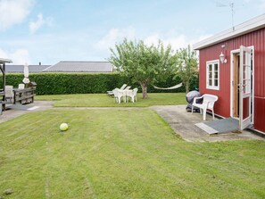 A red building with a door open, a grassy yard, white chairs, and a hammock. - 4 Person Holiday Home in Haderslev-by Traum (Haderslev)