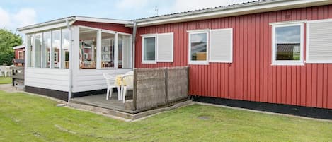 A red mobile home with a covered porch and a small patio area.