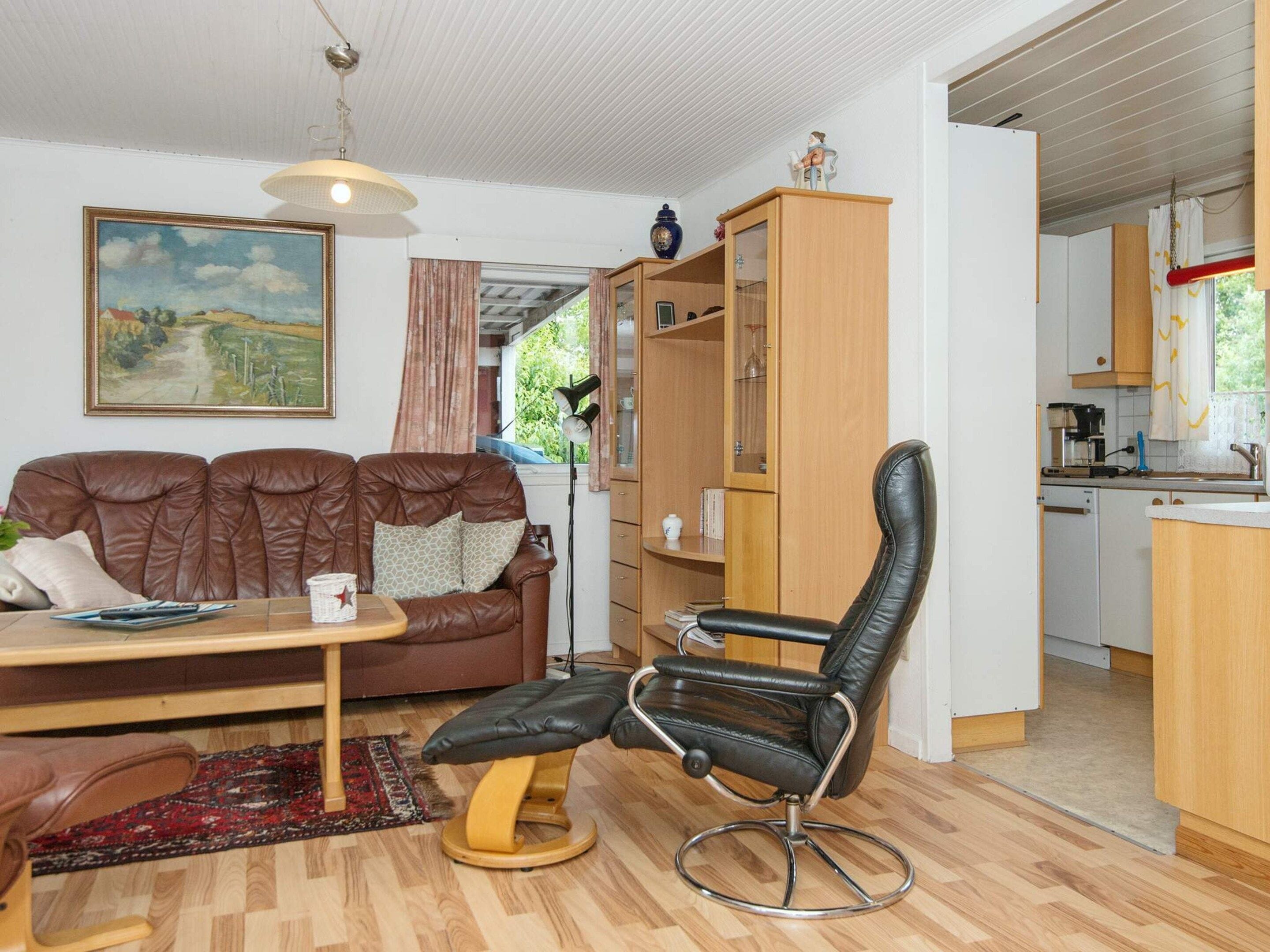 A living room with a brown leather sofa, a black leather chair, a wooden coffee table, and a painting on the wall.