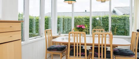 A conservatory with a round table and chairs, large windows, and a view of greenery outside.