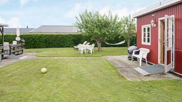 A grassy yard with a red building, white chairs, and a hammock.