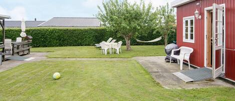 A grassy yard with a red building, white chairs, and a hammock.