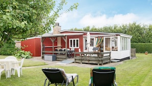 Ein rotes Gebäude mit einer überdachten Terrasse, Sitzgelegenheiten im Freien und einem Rasengrundstück.