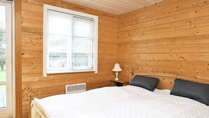 A wooden-paneled bedroom with a bed, a window with blinds, a bedside table with a lamp, and a vent.
