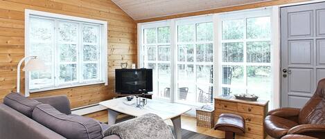 Una habitación acogedora con techo de madera, televisor, sofá, sillón de cuero y ventanas amplias con persianas.