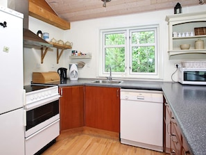 Cocina compacta con armarios de madera, horno empotrado, lavavajillas y ventana con vista a la vegetación.