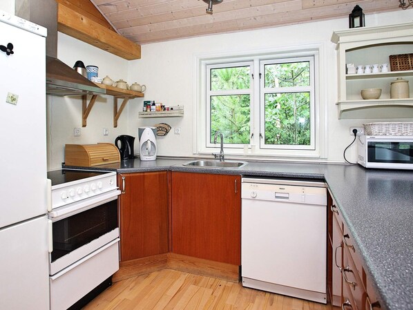 A compact kitchen with wooden cabinets, a built-in oven, a dishwasher, and a window with a view of greenery.