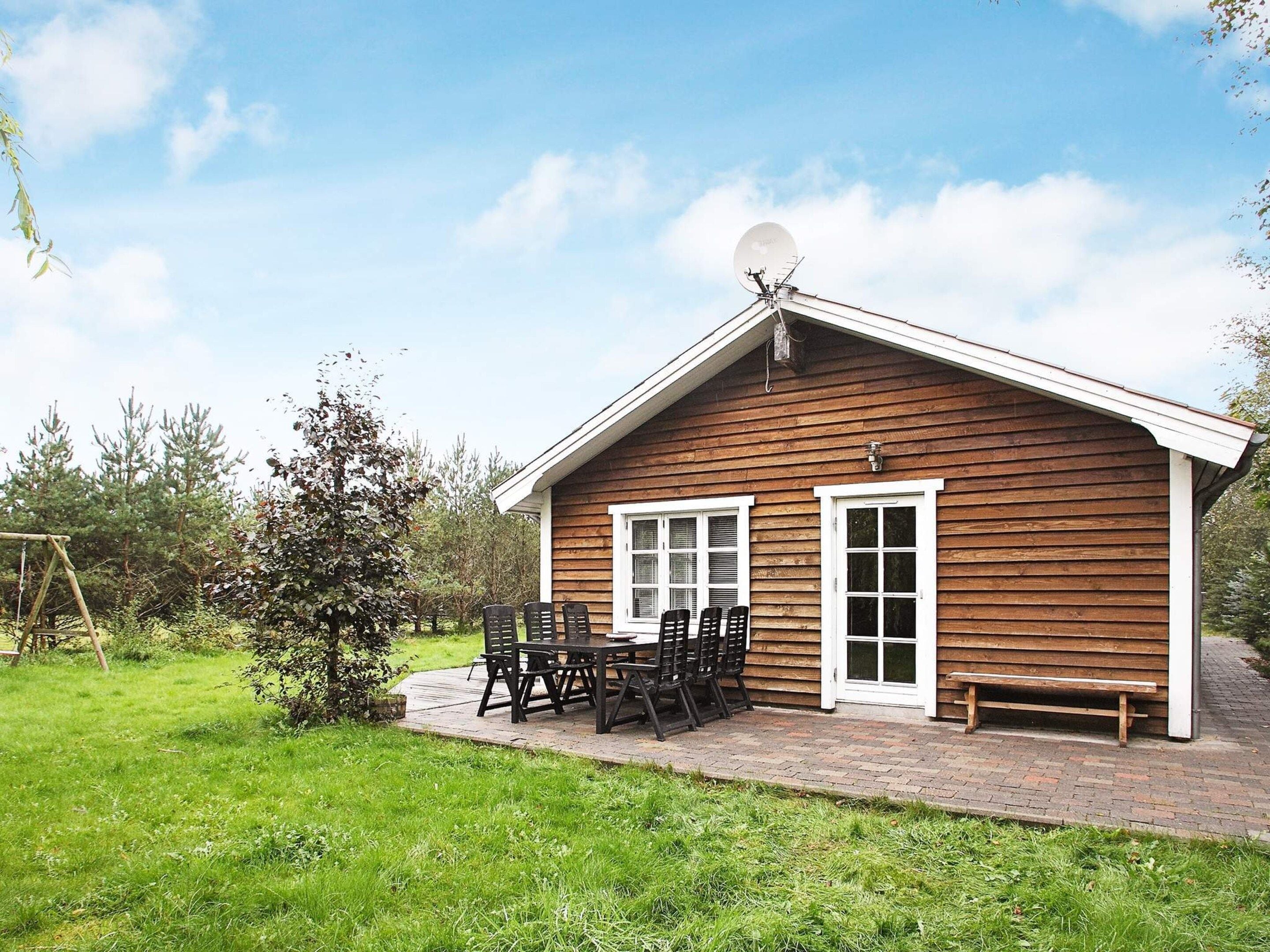 Une cabane en bois avec une antenne parabolique, une terrasse avec une table et des chaises, et un banc.