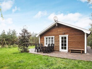A wooden cabin with a satellite dish, a patio with a table and chairs, and a bench.