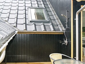 A rooftop with a skylight, a metal shower, and a wicker chair.