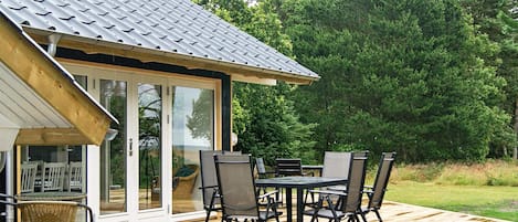 A wooden deck with a table and chairs, a glass door leading to a covered outdoor area, and a metal roof.