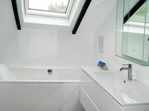 A modern bathroom with a skylight, a bathtub, and a glass-enclosed vanity.