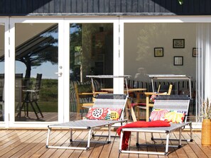 A deck with two lounge chairs and a table, a sliding glass door entrance, and a view of the outdoors.