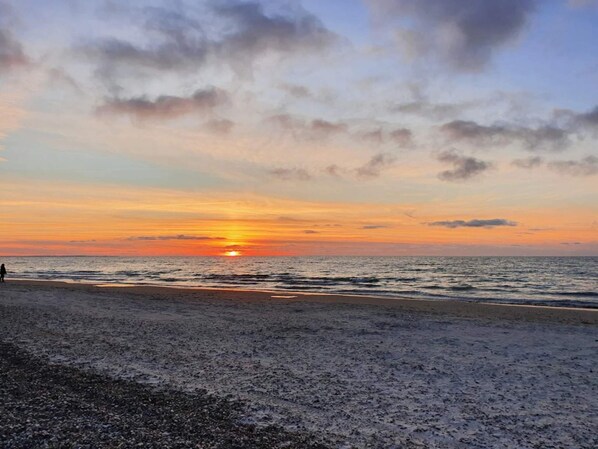 A beach with a sunset, clear sky, and calm sea.