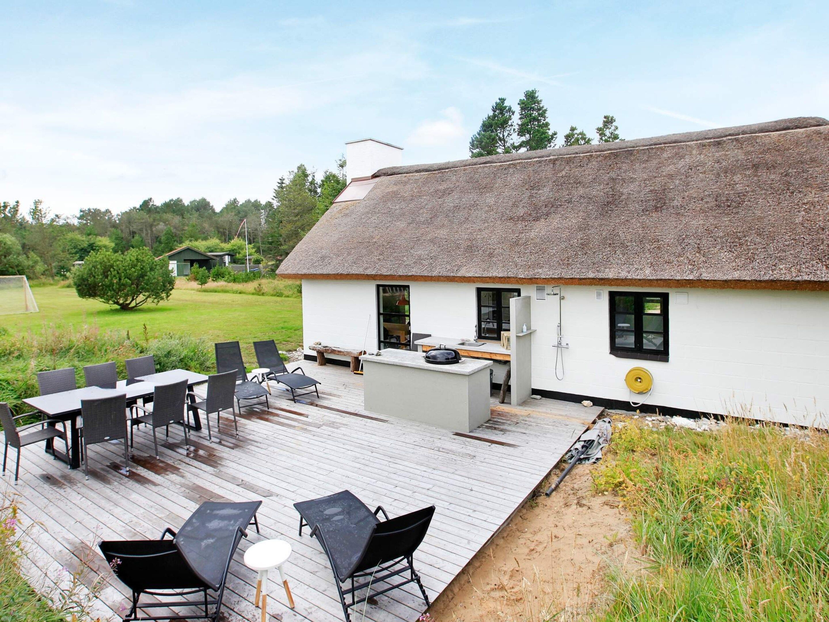 A thatched-roof building with a deck, outdoor seating, and a small kitchen area.