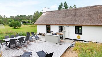 A thatched-roof building with a deck, outdoor seating, and a small kitchen area.