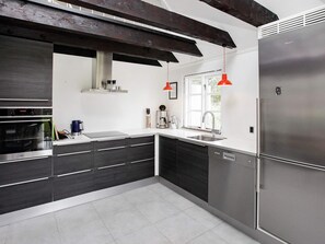 A modern kitchen with a stainless steel refrigerator, a built-in oven, and a window with a view of greenery.