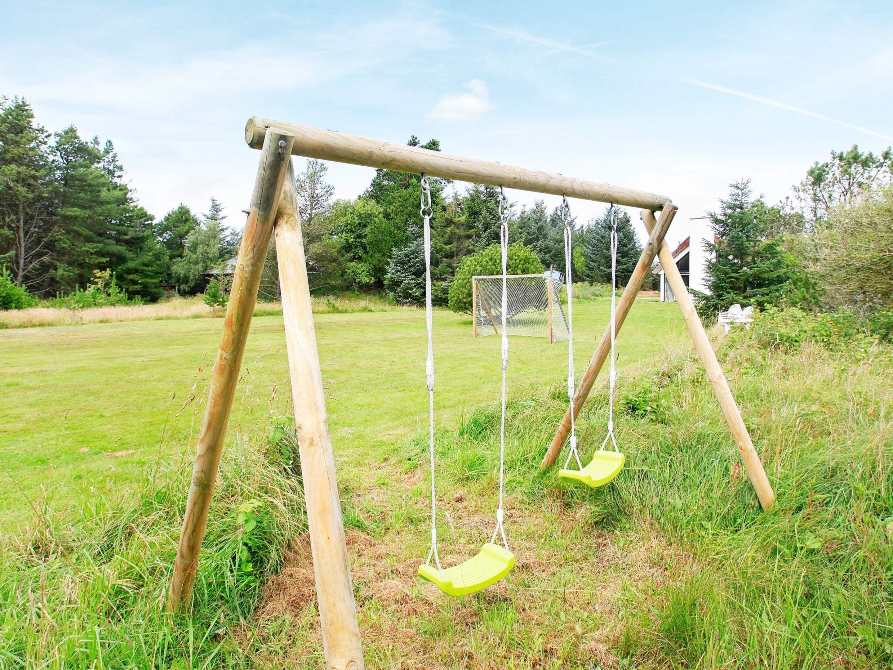 Ein Holzschaukelstuhl in einer grünen Wiese, im Hintergrund Bäume.
