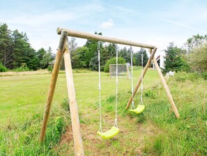 A wooden swing set in a grassy field with trees in the background.