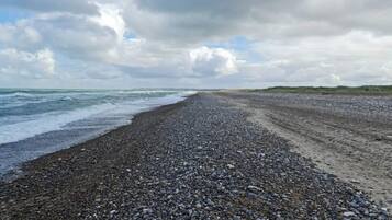 A pebbled beach with waves, a cloudy sky, and distant dunes.