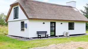A white cottage with a thatched roof, a bench outside, and a small garden area.