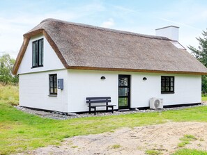 A white cottage with a thatched roof, a bench outside, and a small garden area.