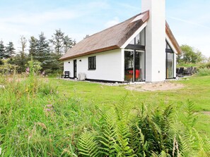 A white building with a thatched roof, a large glass door, and a grassy yard with ferns.