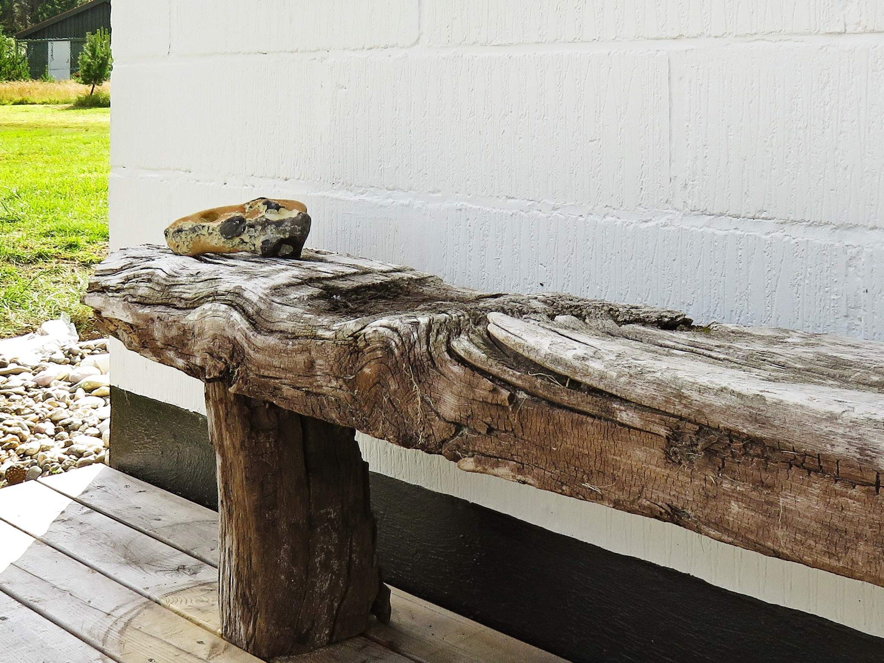 A rustic wooden bench with a stone slab on top, positioned against a white wall.