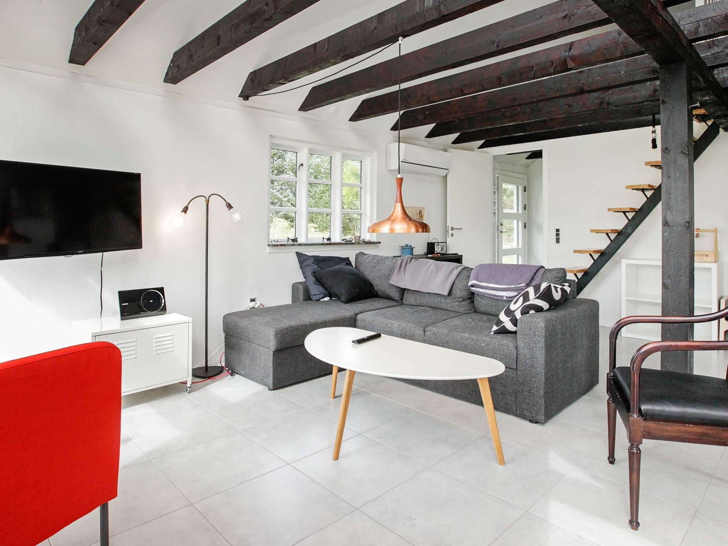 Un salon moderne avec un canapé d’angle, un fauteuil rouge, une table blanche et un escalier.