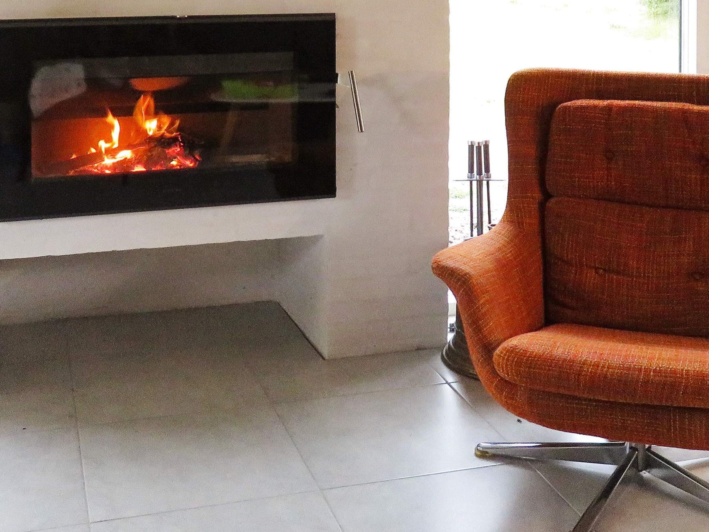 A modern living room with a fireplace, a comfortable orange armchair, and a tiled floor.