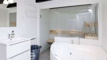 Et moderne badeværelse med en hvid vask, et stort badekar og en brusekabine med glasvægge.