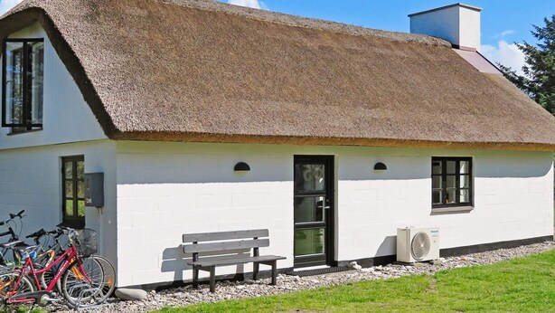 A white building with a thatched roof, a bench, and bicycles parked outside.