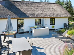 A thatched-roof house with a patio area featuring a table, chairs, and a grill.